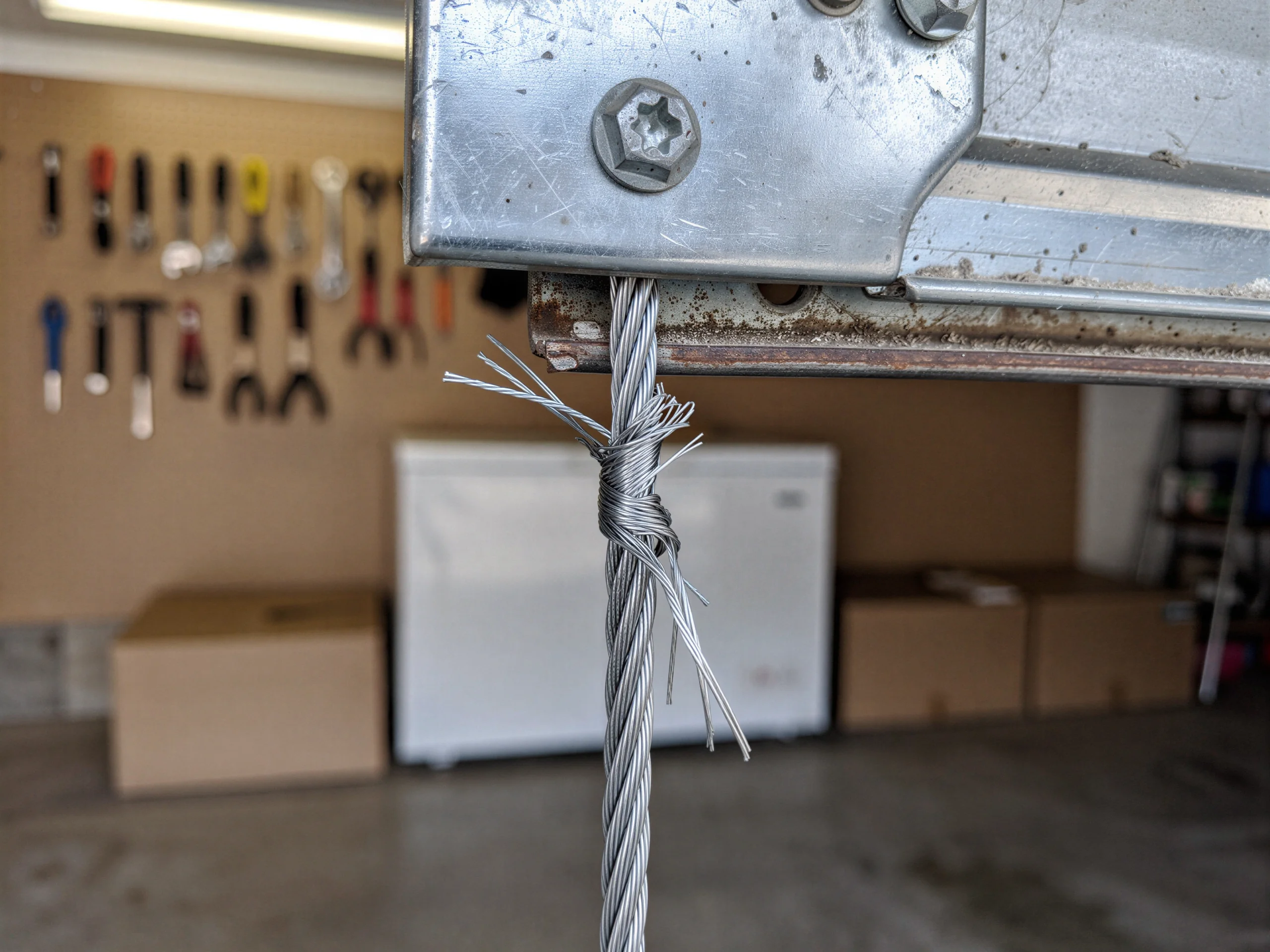 The frayed garage door cable is tied in a knot below a metal bracket.